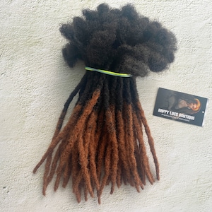 May include: A bundle of brown and black synthetic dreadlocks hair extensions. The dreadlocks are tied together with a rubber band. The text "HAPPY LOCS BOUTIQUE Premium Loc Extensions" is on a black and white business card.