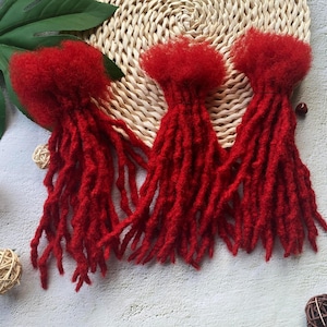 May include: Three red dreadlock extensions with a fluffy texture. The dreadlocks are arranged in a row on a woven surface.