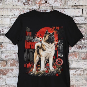Könnte beinhalten: Ein schwarzes T-Shirt mit einer Grafik eines amerikanischen Akita-Hundes, der auf einem Felsen steht. Das Design zeigt eine rote Sonne, Ahornblätter, einen Berg und den Text The furry fortress American Akita. Unten rechts ist eine Pfote abgebildet.