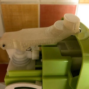 Puede incluir: Primer plano de un dispensador de bomba de plástico blanco con una base verde. La bomba está en posición superior y el dispensador es parcialmente visible.