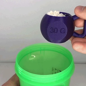 May include: A purple scoop, marked "30 G", holds white powder above a green container. The scoop has a handle. The container is empty and has a wide opening. The scoop is designed to measure 30 grams of powder.