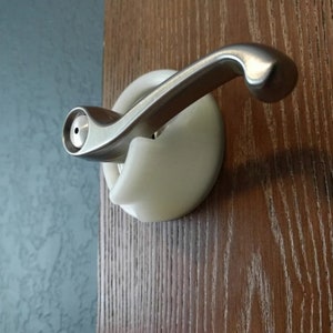 May include: A brushed nickel door handle with a curved lever, mounted on a white backplate. The handle is fixed to a wooden door with vertical grain. The background shows a textured blue wall.
