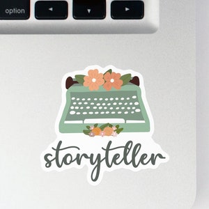 May include: A sticker with a vintage typewriter illustration and the word "storyteller" in cursive. The typewriter is green with a floral design and is surrounded by pink and orange flowers.