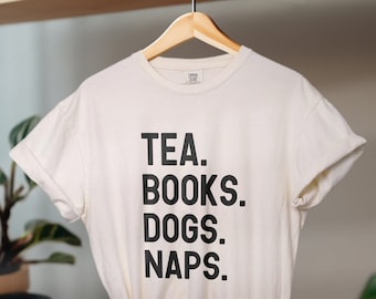 May include: A white t-shirt with black text that reads "TEA. BOOKS. DOGS. NAPS."