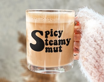 May include: A glass mug filled with a brown liquid. The mug has the text "Spicy Creamy Nut" printed on it in black.