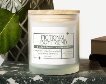May include: A white frosted glass candle jar with a wooden lid. The label reads "Fictional Boyfriend + A Fablebound Crafted Scent" and lists the scent notes: sage, orange, grapefruit, lavender, oakmoss, amber. The candle is hand-poured with vegan coconut soy wax.