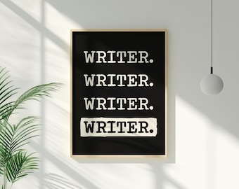 May include: A framed art print featuring the word "WRITER" repeated four times in white against a black background. The top three words are in a simple font, the bottom one on a textured off-white block. The frame is a light wood colour.