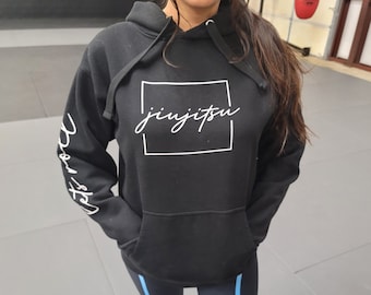 May include: Black hooded sweatshirt with white text that says "jiujitsu" inside a white square. The sleeves have white text that says "Let's roll".