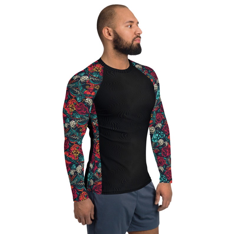 Puede incluir: Camiseta negra de manga larga con estampado floral y calavera de colores en las mangas. La camiseta tiene un fondo negro y un panel de color contrastante en el lateral.