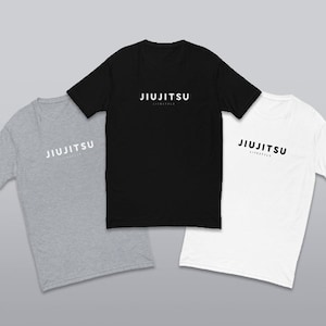 Pode incluir: Três camisetas em cores diferentes: cinza, preto e branco. Cada camiseta tem o texto "Jiu Jitsu Lifestyle" impresso em branco na frente.