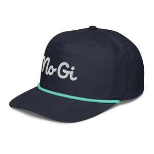 May include: A navy blue baseball cap with a white embroidered logo that says "No Gi" and a turquoise rope trim.