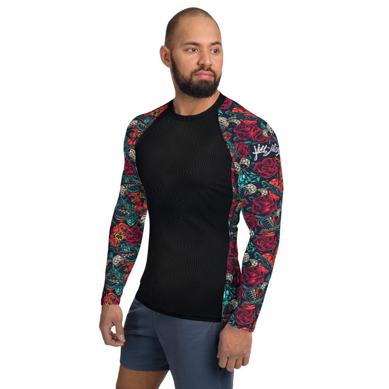 Puede incluir: Camiseta negra de manga larga con un patr&oacute;n floral en las mangas. El patr&oacute;n presenta rosas rojas, hojas verdes y un dise&ntilde;o de calavera. La camiseta tiene cuello redondo y una silueta ajustada.