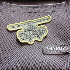May include: A dark grey fabric bag with a green and black helicopter patch and a black patch that says "FLYBOYS GEAR FOR PILOTS".