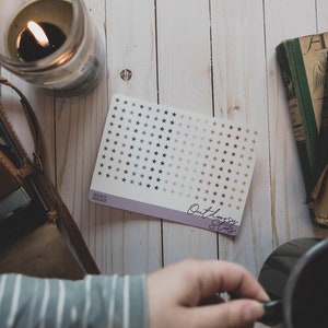 Puede incluir: Una hoja de pegatinas de estrellas con un degradado de estrellas azules, grises y marrones. La hoja de pegatinas está etiquetada como "Outlaw Stars" y está sobre una superficie de madera blanca.