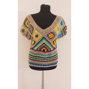 May include: A crocheted top with a geometric pattern in shades of blue, yellow, green, orange, purple, and brown. The top has a V-neck and short sleeves.