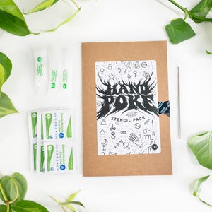 May include: A brown stencil pack with the text "HAND POKE STENCIL PACK" and various black and white illustrations. Also included are sterile alcohol prep pads and a metal tool. Green plants surround the items.