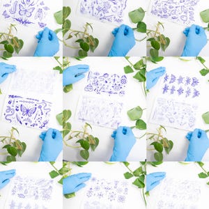May include: A collection of twelve images featuring blue-ink illustrations on white paper. Each image showcases a different design, including butterflies, flowers, and other decorative elements. The images are arranged in a grid, with a hand in a blue glove holding each one.