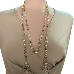 Peut inclure: Long collier à plusieurs rangs orné de fausses perles blanches et mauves, entrecoupées de maillons de chaîne dorés et de pendentifs floraux. Le collier est présenté sur un mannequin.