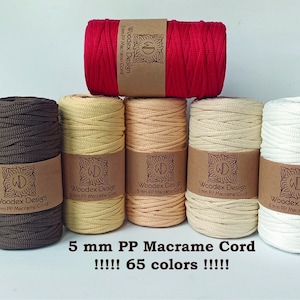 May include: Five spools of 5 mm PP macrame cord in brown, yellow, beige, cream, and white. The spools are arranged in a pyramid shape. The label on each spool reads "Woodex Design 5 mm PP Macrame Cord". The text below the spools reads "5 mm PP Macrame Cord !!!!! 65 colors !!!!!".