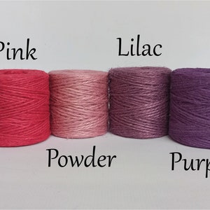 Op de afbeelding: Vier strengen touw in de kleuren roze, poeder, lila en paars. De kleuren zijn gelabeld met de bijbehorende namen. Het touw is strak opgerold in cilindrische vormen, perfect voor knutsel- en decoratieprojecten.