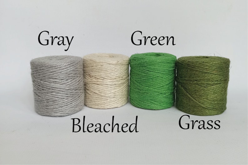 Op de afbeelding: Vier strengen touw in verschillende kleuren: grijs, gebleekt, groen en grasgroen. Elke streng is gelabeld met de kleurnaam. Het touw is strak opgerold, geschikt voor knutselen of verpakken.