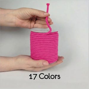 Pode incluir: Uma bobina de cordão rosa choque enrolado em formato cilíndrico. O cordão é feito de material trançado e está enrolado firmemente em torno de um núcleo central. O texto 17 Colors está impresso em preto na parte inferior da imagem.