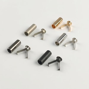 May include: A collection of four sets of metal cord ends and matching fasteners in gold, silver, gunmetal, and matte black finishes. Each set consists of a hollow cylindrical tube and a corresponding pronged insert piece for securing cords.