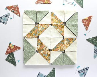 May include: A quilt block in progress, featuring a star pattern with green, white, and yellow fabric squares. The fabric squares are pinned together with safety pins.