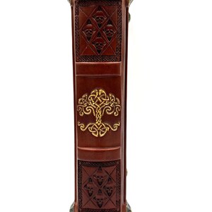 Op de afbeelding: De rug van een bruin lederen gebonden boek met gouden reli&euml;fmotieven. De motieven omvatten een levensboom en een herhalend patroon van schedels.