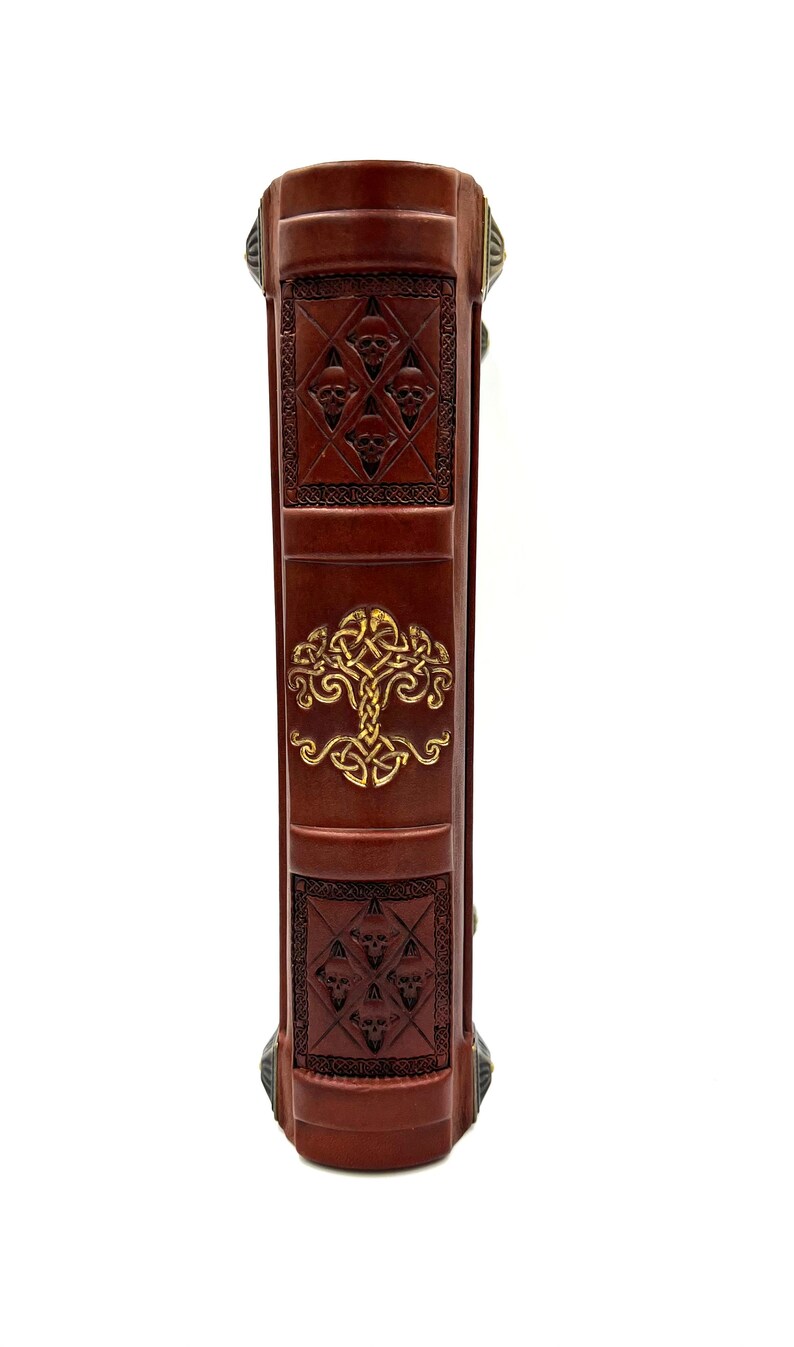 Op de afbeelding: De rug van een bruin lederen gebonden boek met gouden reli&euml;fmotieven. De motieven omvatten een levensboom en een herhalend patroon van schedels.