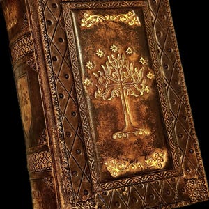 May include: A detailed, antique-style book with a brown leather cover. The cover features a gold embossed tree design with stars, and ornate gold borders. The book's spine and edges are also intricately decorated, creating a vintage aesthetic.