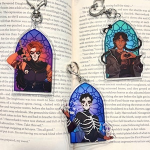 May include: Clear acrylic keychains featuring character art in a stained-glass window design. The keychains depict characters with unique facial markings and attire, holding weapons or skulls. The color palette includes orange, black, and blue.