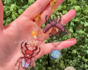 May include: Clear acrylic keychains featuring insect designs, including a red stag beetle, a brown beetle, and a sun. The keychains have gold-colored hardware and the text "APOTHECARYOCTOPUS".