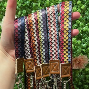 May include: Several colorful lanyards with a scale pattern in shades of blue, purple, red, yellow, and orange. Each lanyard has a brown leather accent and a silver-colored clasp.