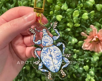 May include: A blue and white patterned beetle keychain with a gold metal ring. The beetle is made of clear acrylic and has a detailed design.