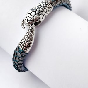 May include: A silver snake bracelet with a textured leather band. The snake's head is a clasp.