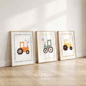 May include: Three framed wall art prints featuring tractors in orange, green, and yellow. Each print displays a tractor with smoke, enclosed by a dashed border. The frames are light wood, and the artwork is displayed in a row on a light floor.
