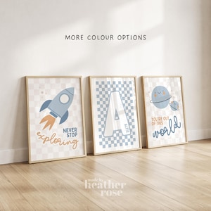 May include: Three framed wall art prints featuring a space theme with a light blue and beige checkered background. The first print shows a rocket with the text NEVER STOP exploring. The second shows a large letter A with the name ALFIE. The third shows planets with the text YOU'RE OUT OF THIS world.