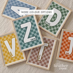 May include: Six framed rectangular wall prints featuring a checkered background in various colours including blue, green, yellow, teal, brown, and orange. Each print displays a large white capital letter and a name printed in black text.