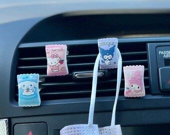 May include: A car's interior with a dashboard featuring a screen and controls.  There are several small, colorful, cartoon character air fresheners hanging from the air vents.  A white and light pink face mask is hanging from the vent on the driver's side.