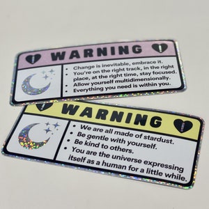 Puede incluir: Dos pegatinas de advertencia con un dise&ntilde;o de luna creciente y estrellas. La primera pegatina es rosa con el texto "El cambio es inevitable, ac&eacute;ptalo. Est&aacute;s en el camino correcto, en el lugar correcto, en el momento correcto, mantente concentrado. Perm&iacute;tete ser multidimensional. Todo lo que necesitas est&aacute; dentro de ti." La segunda pegatina es amarilla con el texto "Todos estamos hechos de polvo de estrellas. S&eacute; amable contigo mismo. S&eacute; amable con los dem&aacute;s. T&uacute; eres el universo que se expresa como un humano por un tiempo."