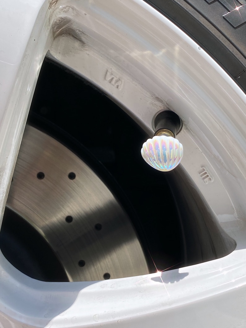 May include: Close-up of a white car tire with a iridescent seashell-shaped valve stem cap. The tire is mounted on a white rim with the number "7.5" visible.