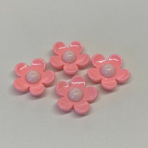 May include: Four pink plastic flower-shaped buttons with white centers.