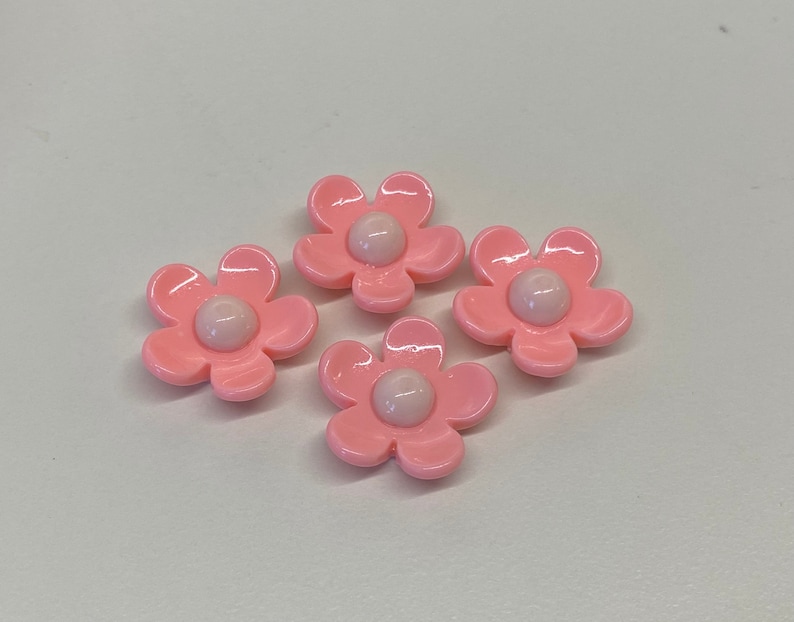 May include: Four pink plastic flower-shaped buttons with white centers.