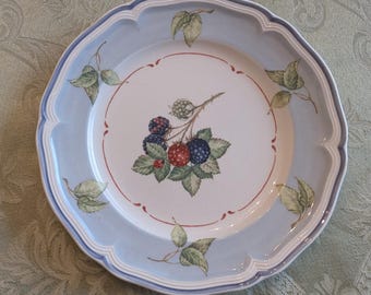 May include: A blue and white ceramic dinner plate with a decorative design of blackberries and leaves. The plate has a scalloped edge.