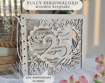 May include: A square wooden keepsake with a laser-cut heart design featuring the number 25 in the centre, surrounded by floral patterns. The cover is bound with white string on the left side and displays printed text on the inner page.