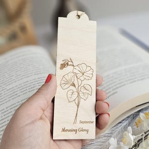 May include: A wooden bookmark featuring an engraved Morning Glory plant design. The bookmark has a rounded top with a string. The text "September Morning Glory" is engraved on the bookmark. A decorative item for book lovers.