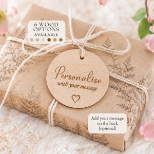 May include: A round light-coloured wooden gift tag tied with twine to a rectangular package wrapped in brown paper with a fern print. The tag features the engraved text "Personalise with your message" and a small heart icon. A label indicates 6 wood options.