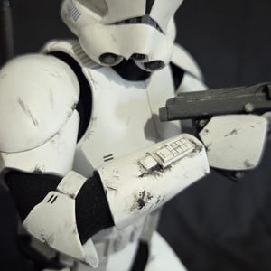 May include: A white and black Stormtrooper armor costume with a blaster rifle. The costume has visible wear and tear, suggesting a battle-worn appearance. The helmet and armor plates are detailed.