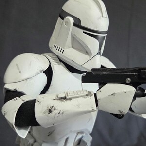 May include: A white and black Clone Trooper helmet and armor, with a blaster rifle. The armor has black accents and visible wear and tear. The helmet has a distinctive design with a visor and antenna.